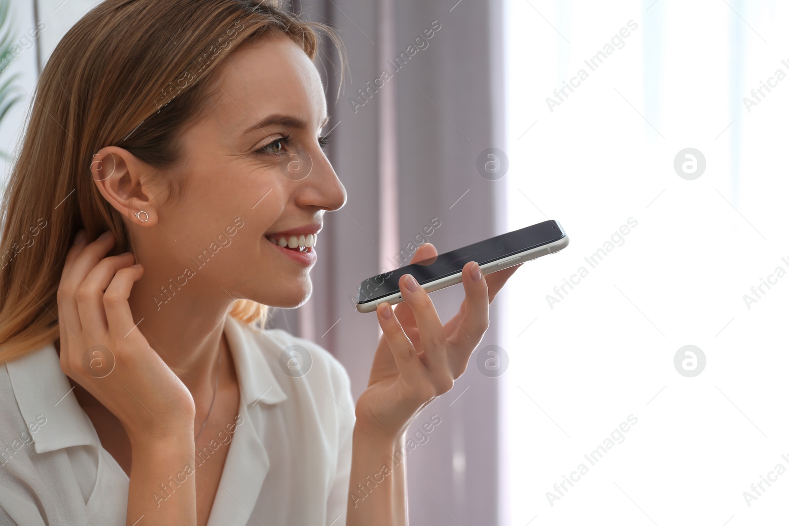 Photo of Young woman using voice search on smartphone indoors