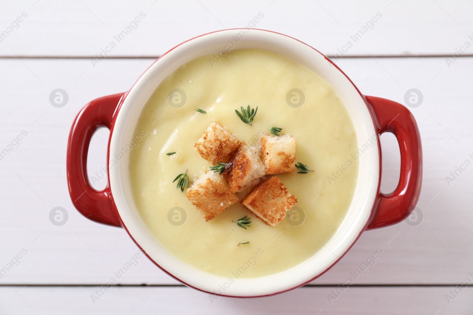 Photo of Tasty potato soup with croutons and rosemary in ceramic pot on white wooden table, top view