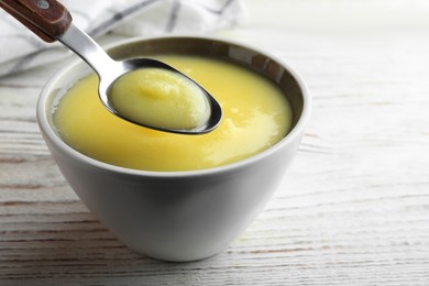 Photo of Bowl and spoon of Ghee butter on white wooden table, closeup