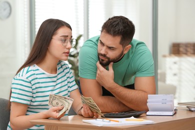 Photo of Worried young couple counting money at wooden table indoors