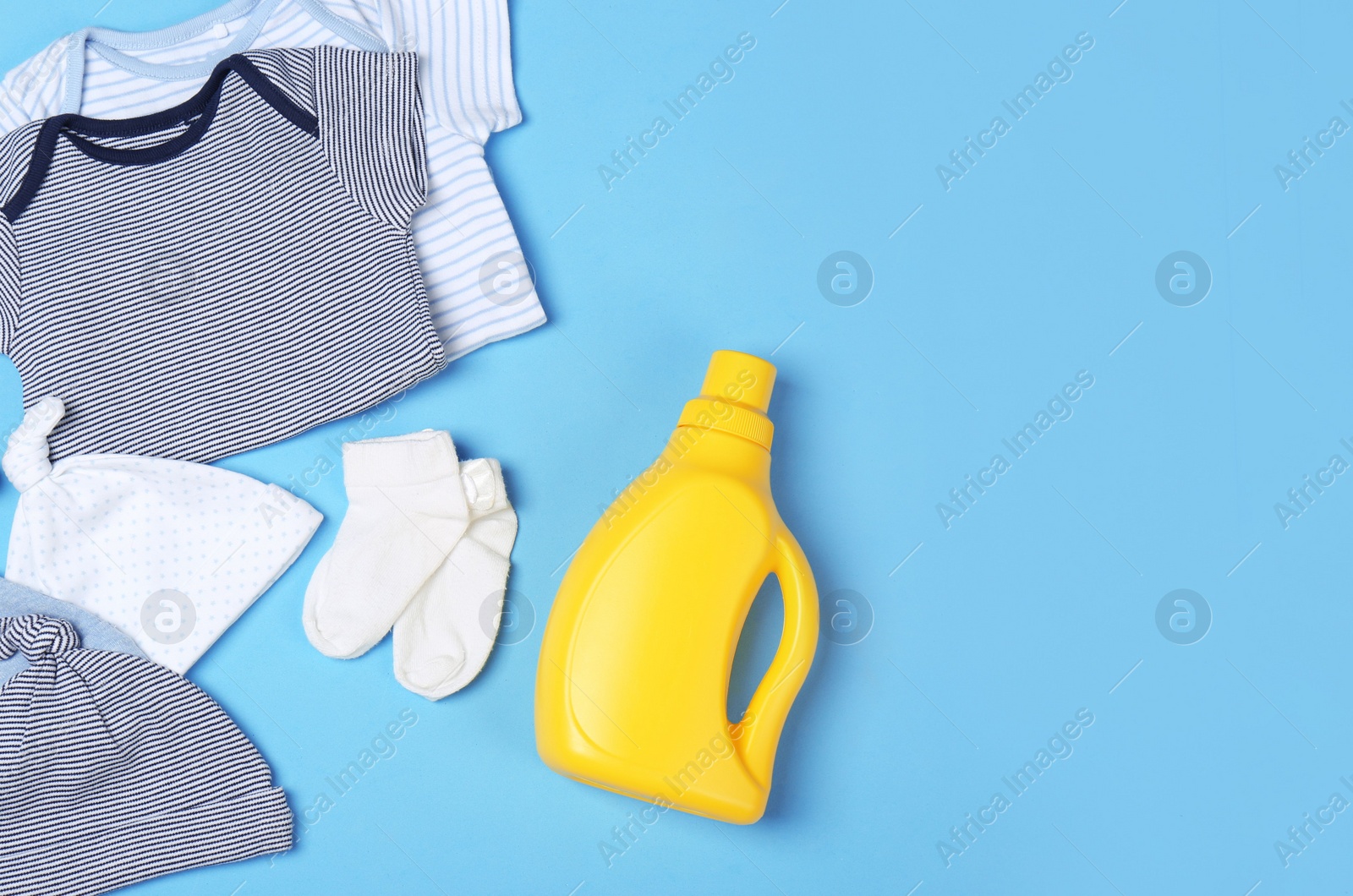 Photo of Flat lay composition with bottle of detergent and children's clothes on light blue background