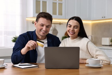 Photo of Happy couple with laptop and credit card shopping online at wooden table in kitchen