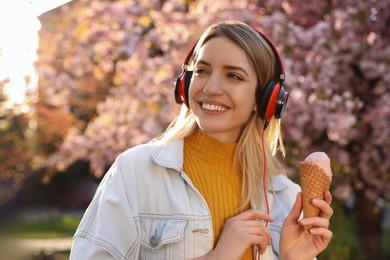 Young woman with ice cream and headphones listening to music outdoors on sunny day