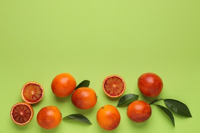 Photo of Many ripe sicilian oranges and leaves on light green background, flat lay. Space for text