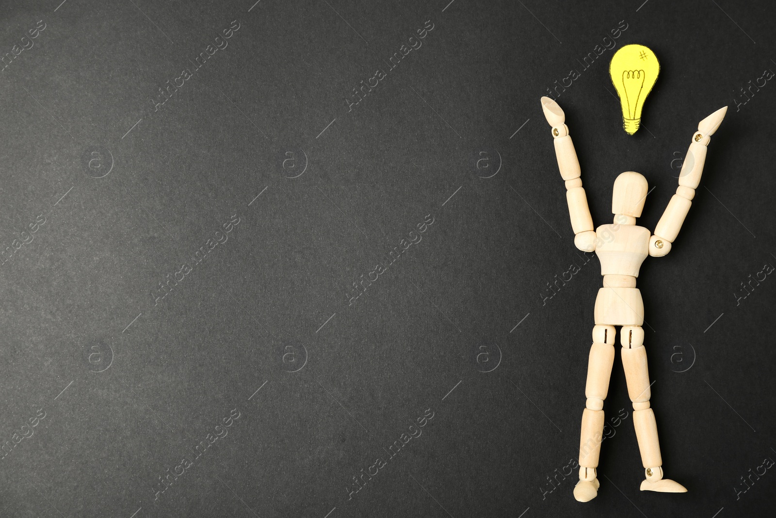 Photo of Wooden puppet and paper lightbulb on black background, flat lay. Space for text