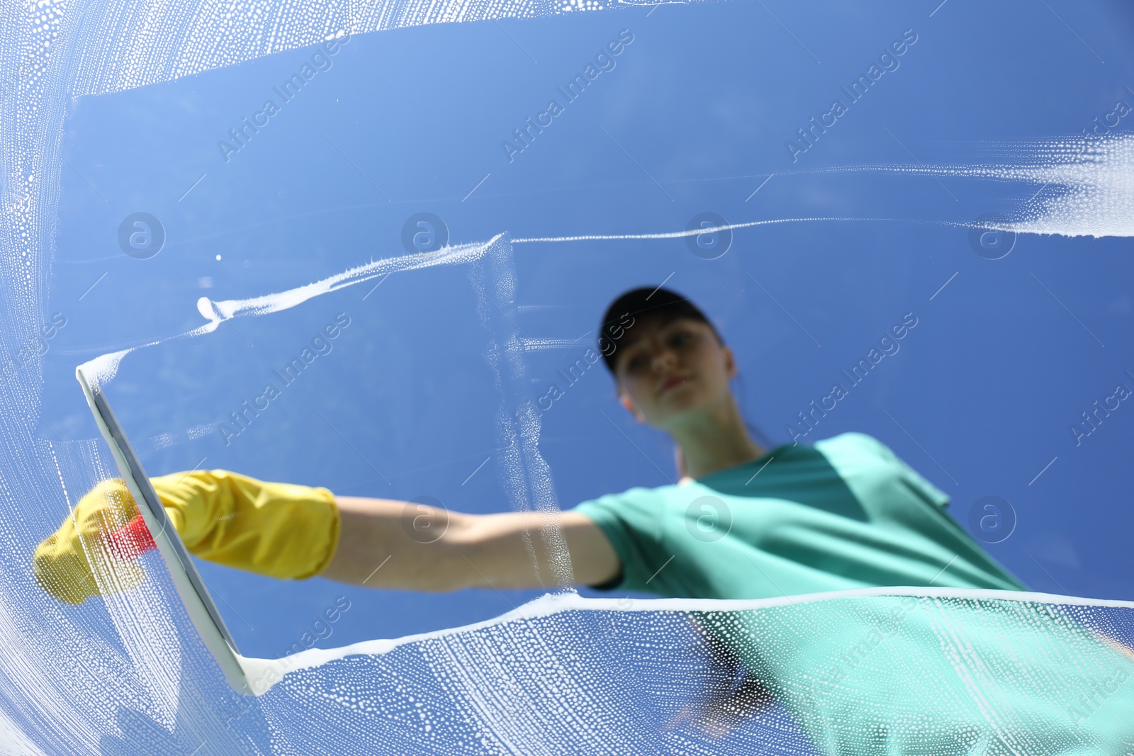 Photo of Woman cleaning glass with squeegee on sunny day