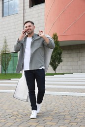 Man holding garment cover with clothes outdoors. Dry-cleaning service