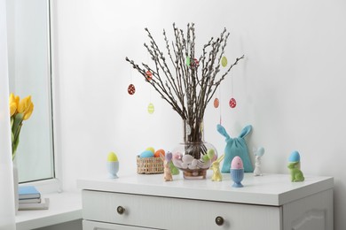 Beautiful pussy willow branches with paper eggs in vase and Easter decor on white chest of drawers at home