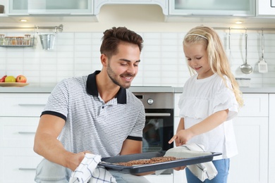 Young man treating his daughter with homemade oven baked baked cookies in kitchen