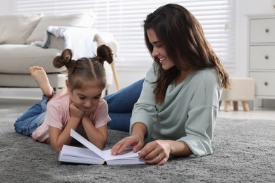 Photo of Young mother and her daughter reading book on floor at home