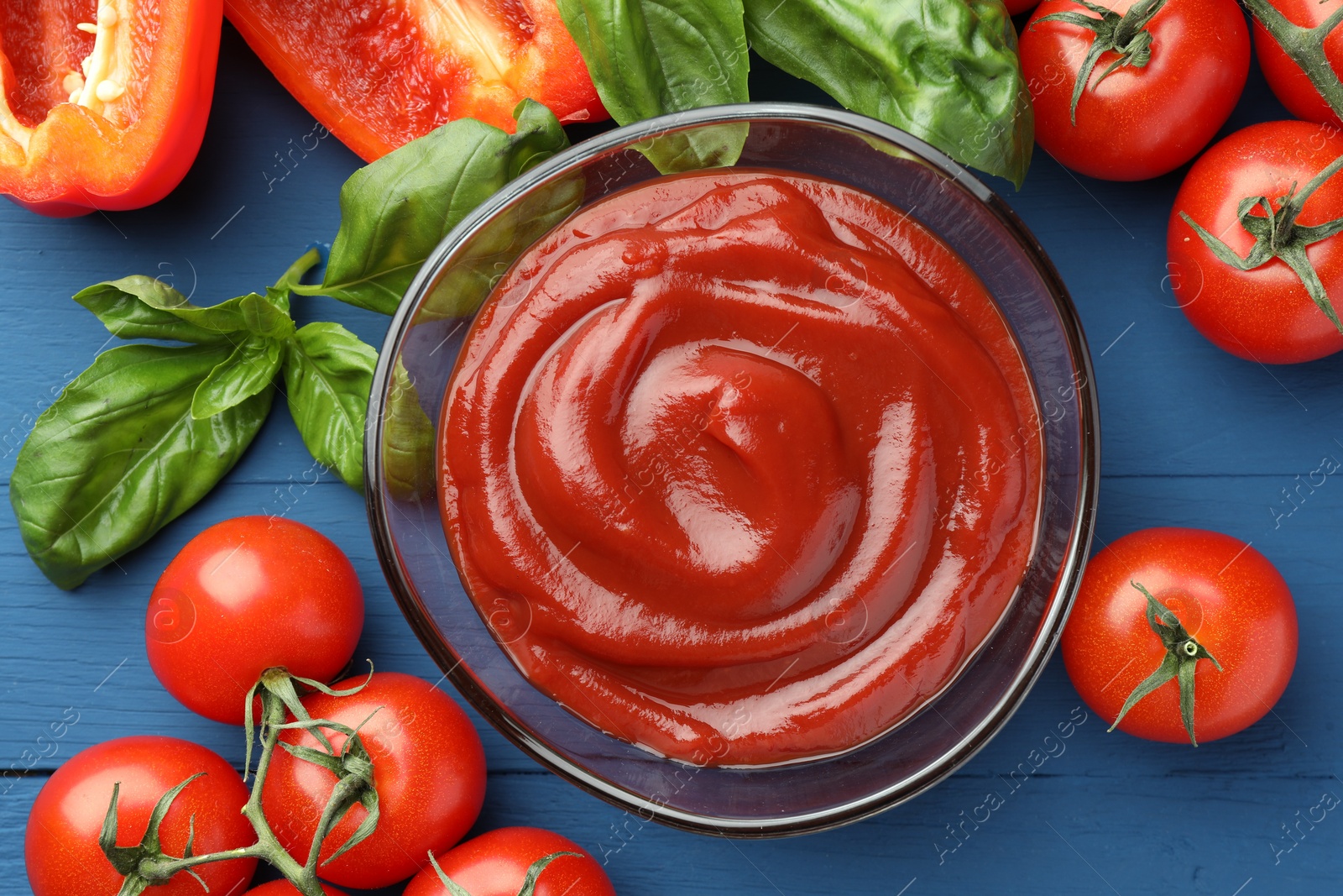 Photo of Bowl of tasty ketchup and ingredients on blue wooden table, flat lay