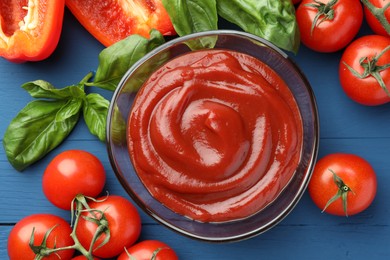 Photo of Bowl of tasty ketchup and ingredients on blue wooden table, flat lay