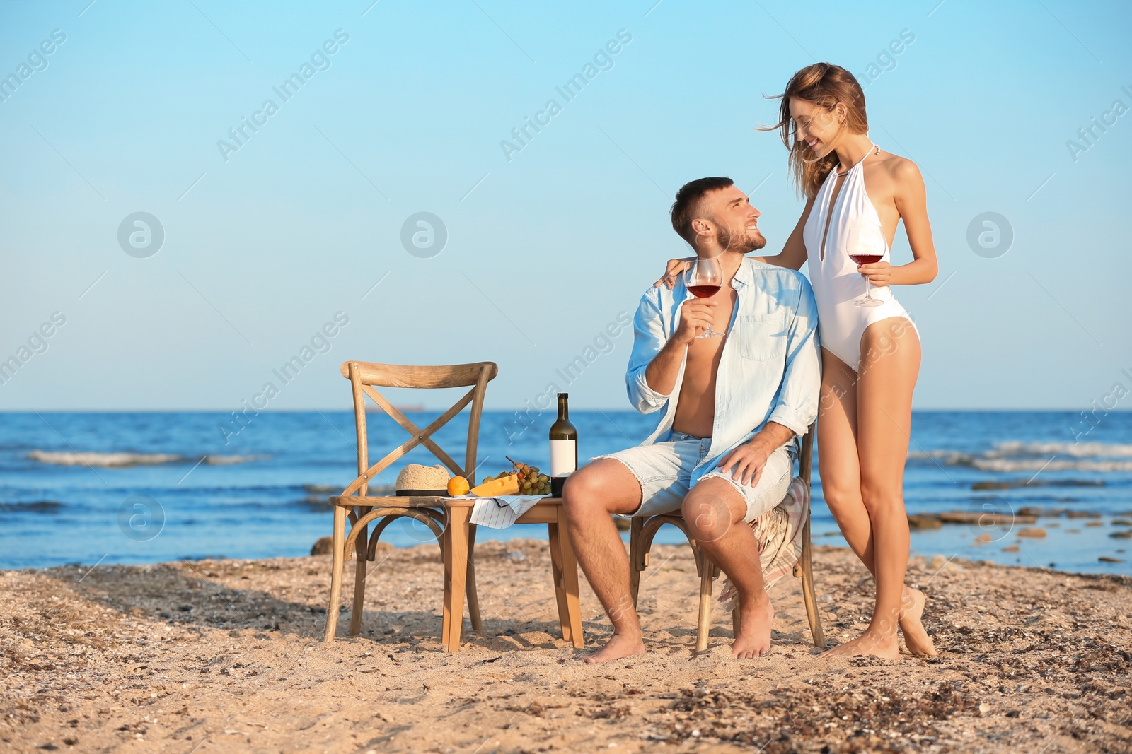 Photo of Young couple with glasses of wine having romantic dinner on beach