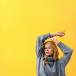 Beautiful young woman wearing warm blue sweater on yellow background. Space for text