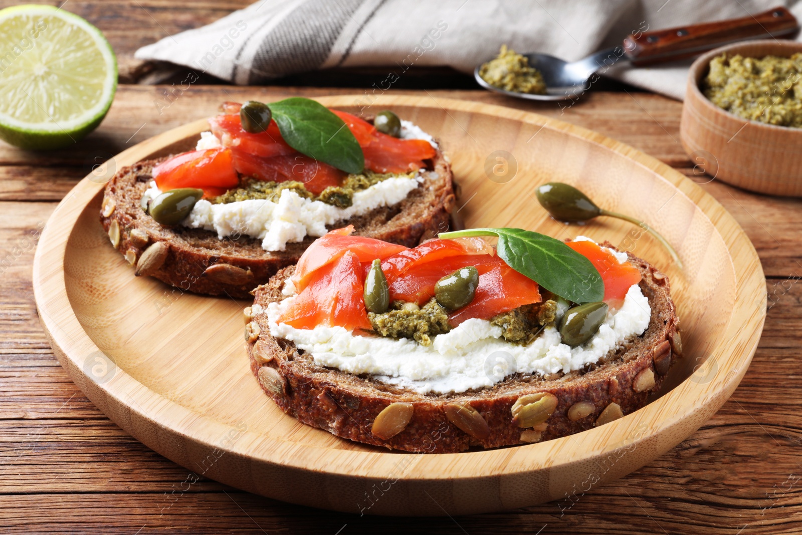 Photo of Delicious sandwiches with cream cheese, salmon, capers and pesto on wooden table
