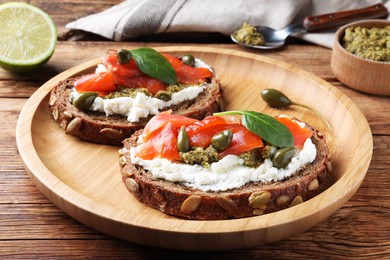 Delicious sandwiches with cream cheese, salmon, capers and pesto on wooden table