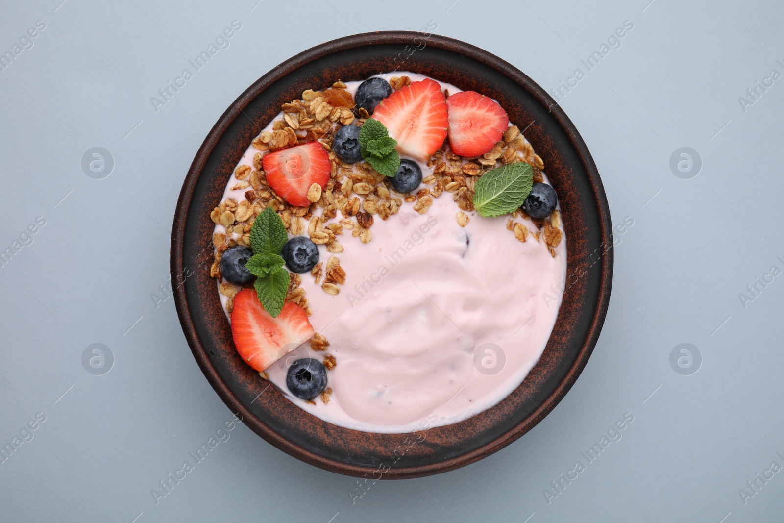 Photo of Bowl with yogurt, berries and granola on light grey background, top view