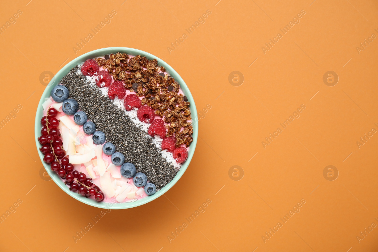 Photo of Tasty smoothie bowl with fresh berries and granola on orange background, top view. Space for text