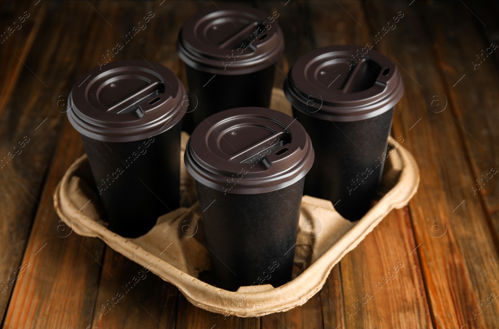 Photo of Takeaway paper coffee cups in cardboard holder on wooden table