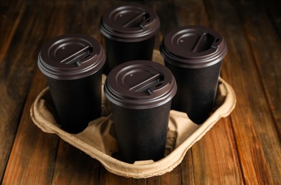 Takeaway paper coffee cups in cardboard holder on wooden table