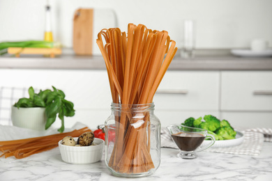 Photo of Uncooked buckwheat noodles and fresh ingredients  on white marble table in kitchen