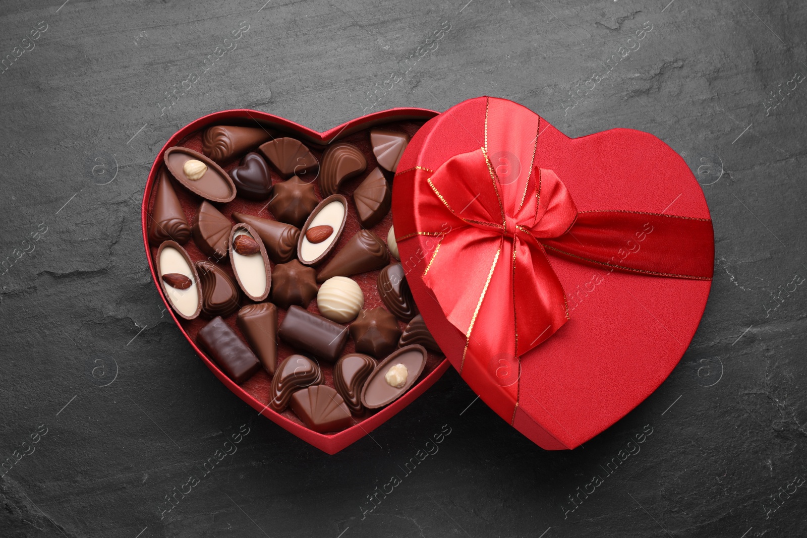 Photo of Heart shaped box with delicious chocolate candies on black table, top view
