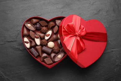 Photo of Heart shaped box with delicious chocolate candies on black table, top view