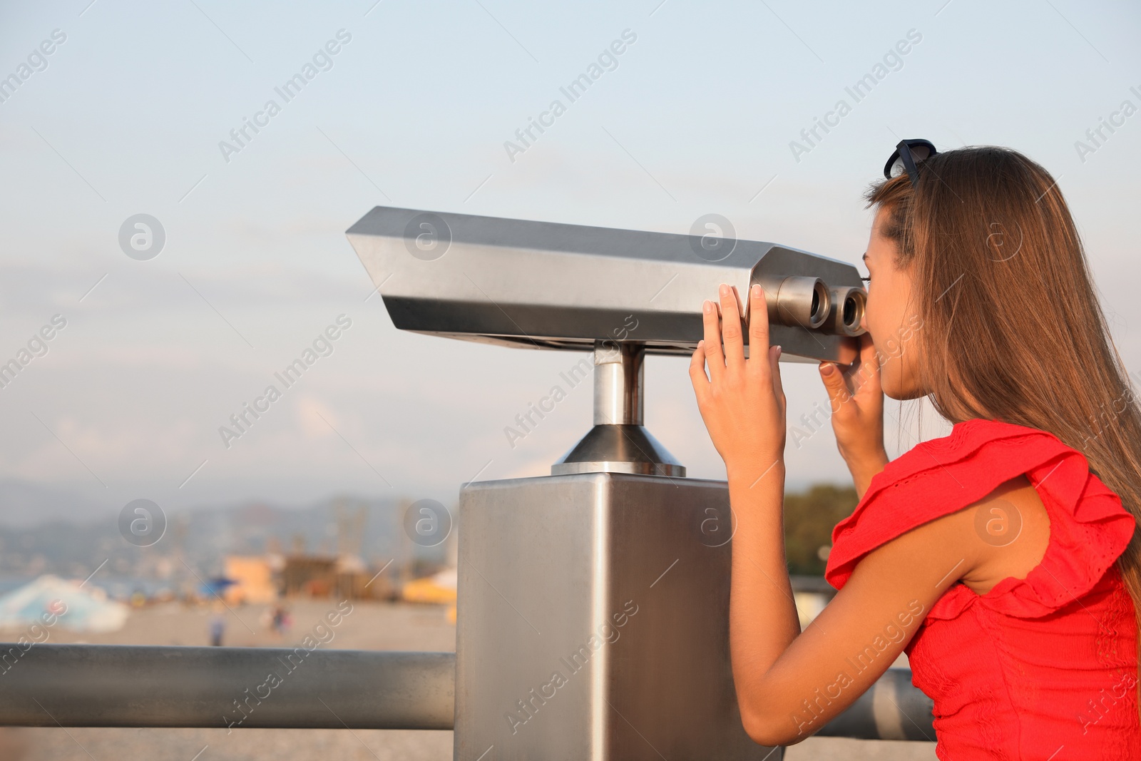 Photo of Young woman looking through tourist viewing machine at observation deck