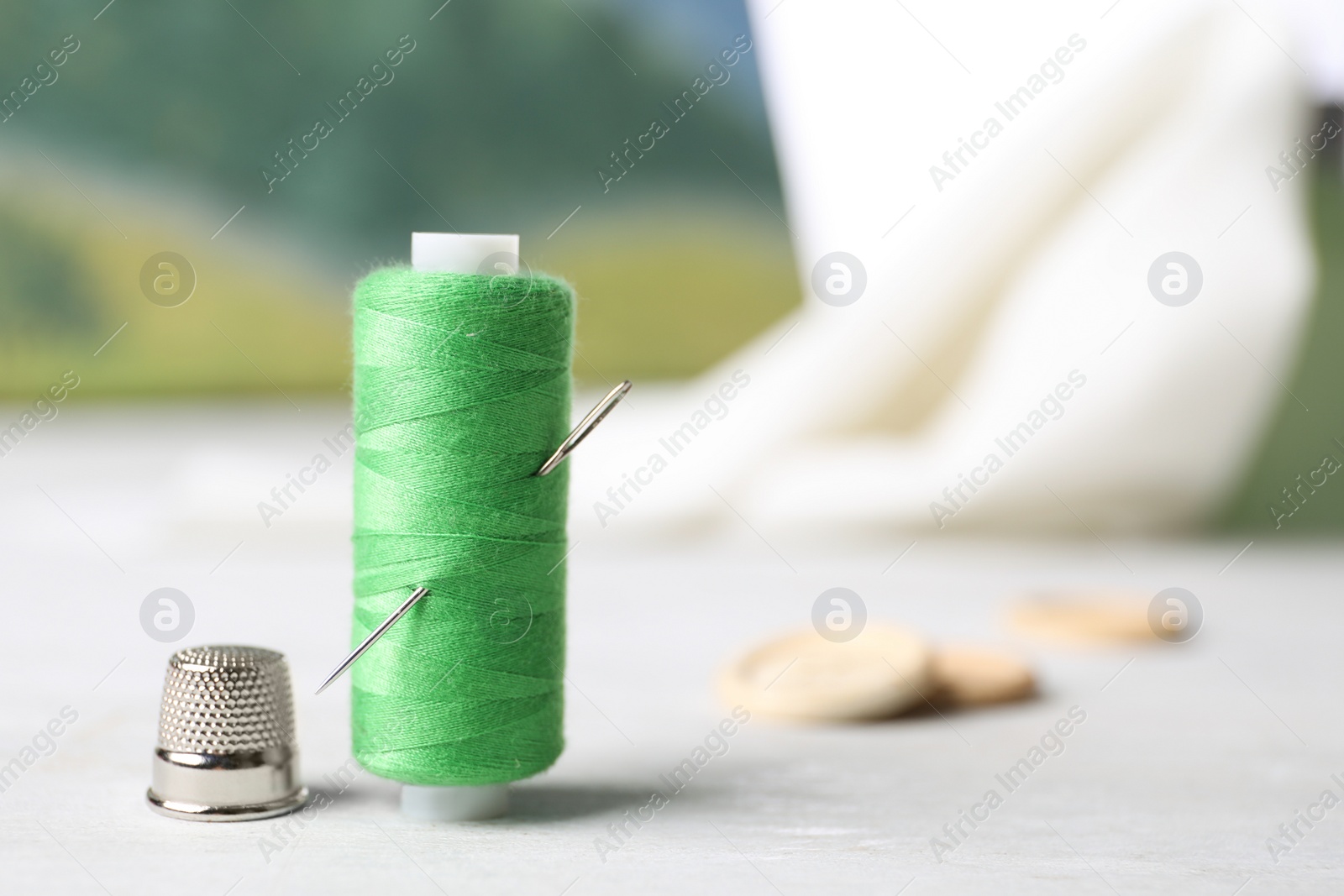 Photo of Spool of green sewing thread with needle and thimble on white table, space for text
