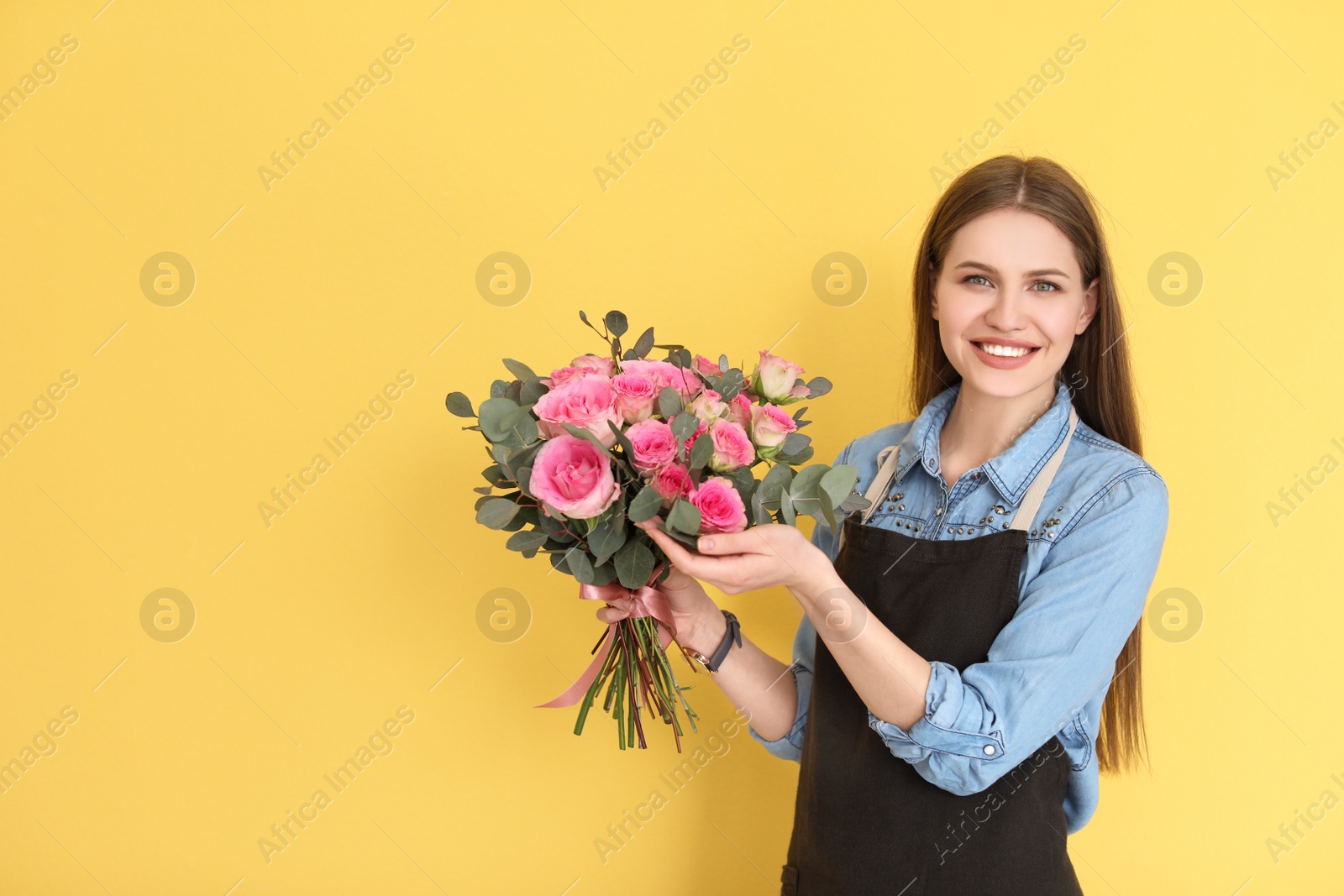 Photo of Female florist holding bouquet of beautiful flowers on color background