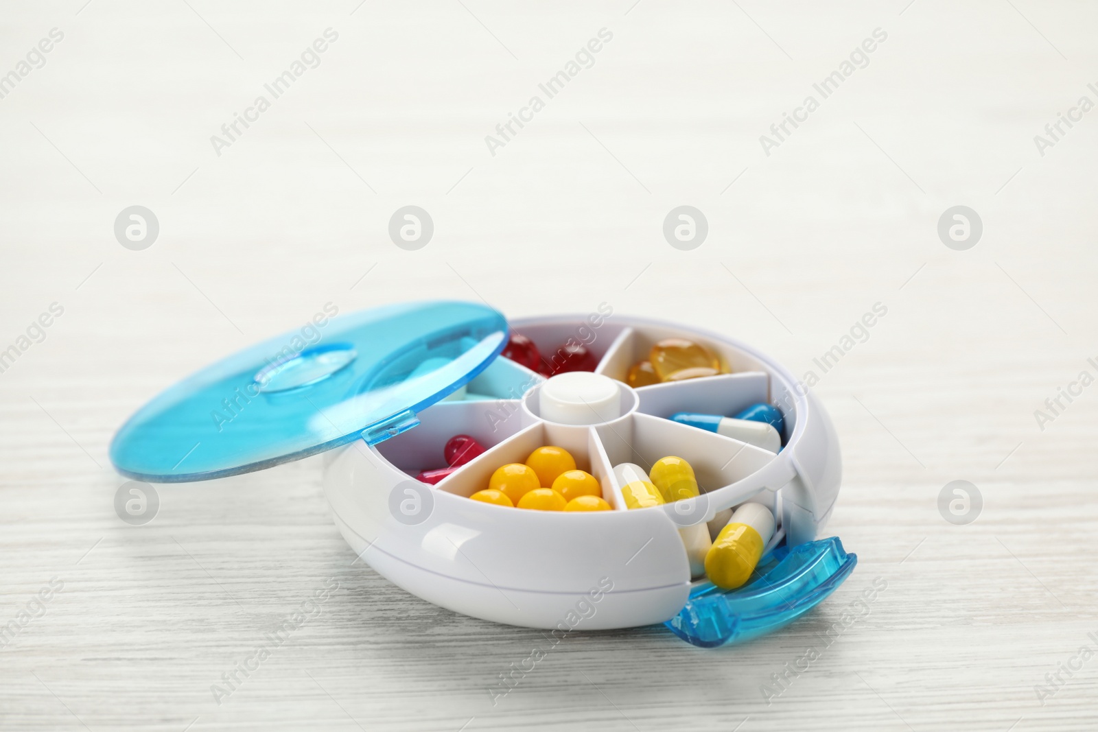 Photo of Plastic box with different pills on white wooden table