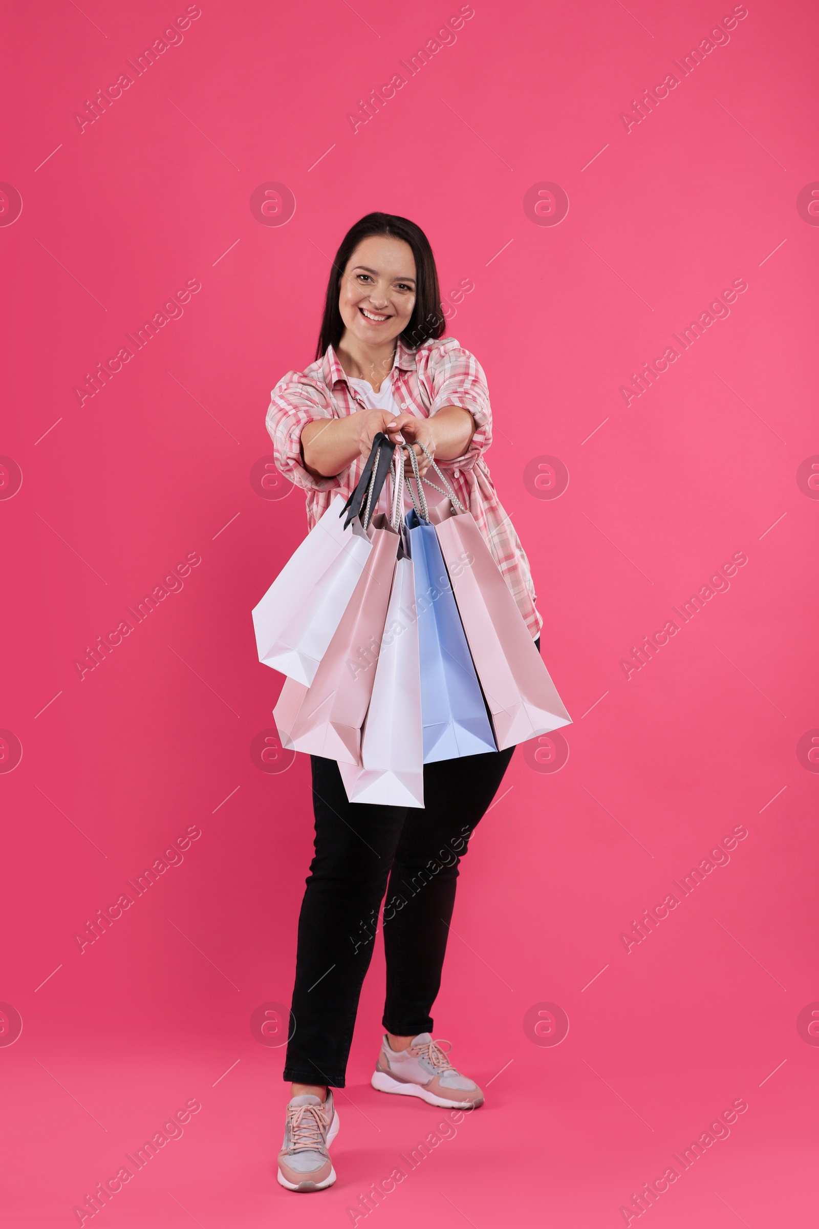 Photo of Beautiful overweight woman with shopping bags on pink background