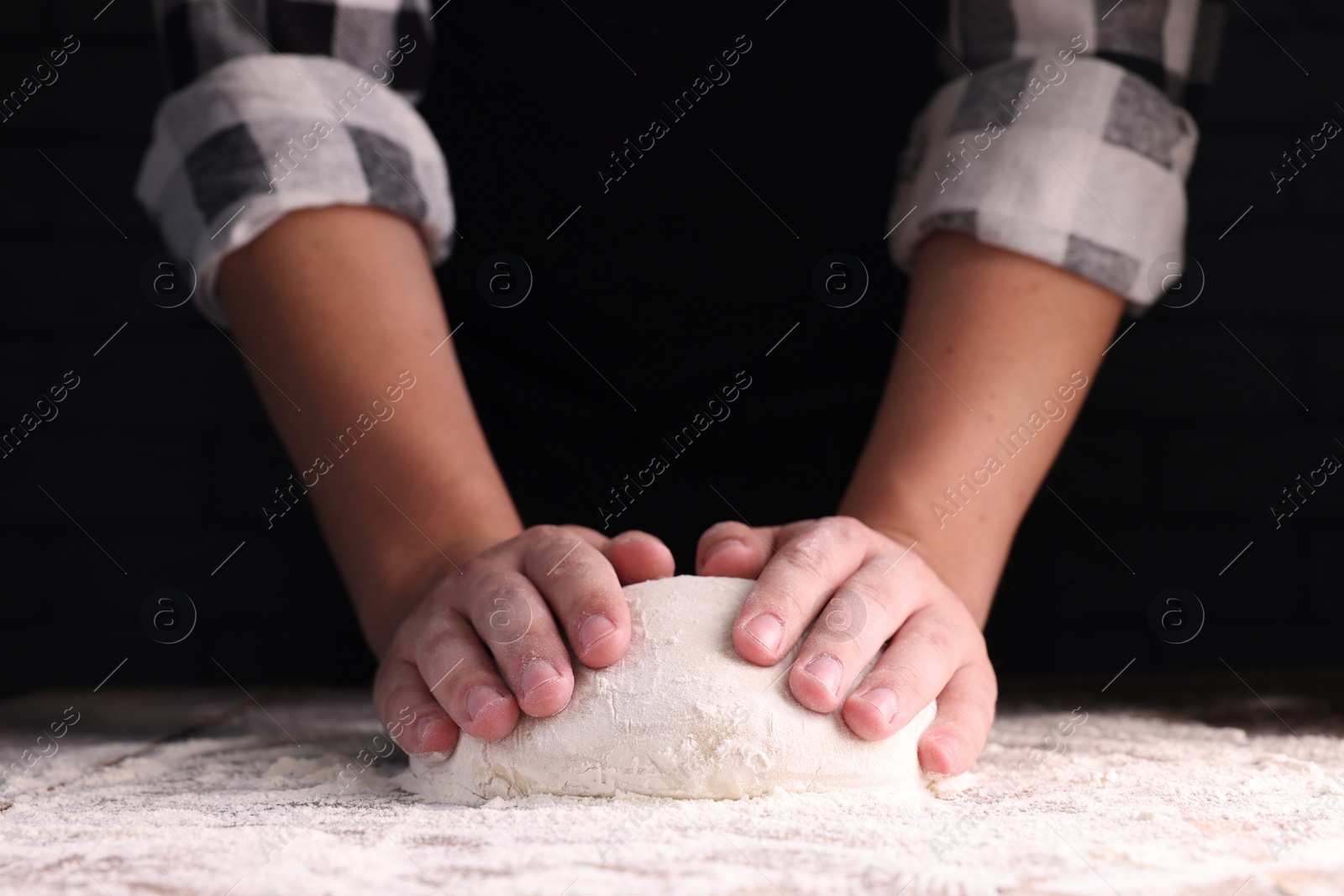 Photo of Man kneading dough at wooden table on dark background, closeup