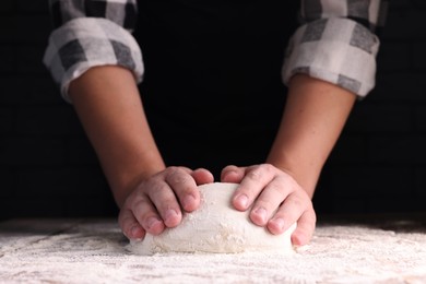 Photo of Man kneading dough at wooden table on dark background, closeup