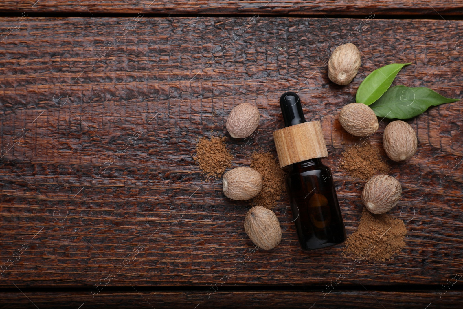 Photo of Bottle of nutmeg oil, nuts and powder on wooden table, flat lay. Space for text