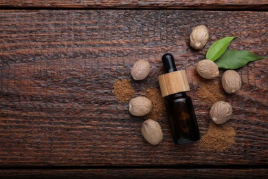 Photo of Bottle of nutmeg oil, nuts and powder on wooden table, flat lay. Space for text