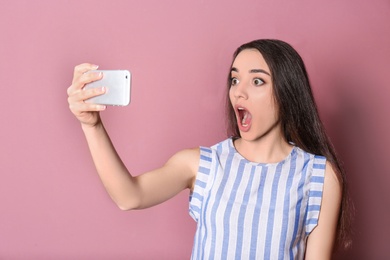 Young beautiful woman taking selfie against color background