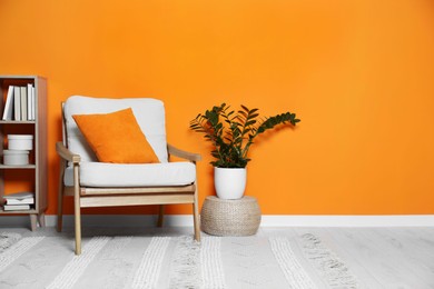 Photo of Cosy armchair, wooden rack and potted plant near orange wall in room, space for text. Interior design