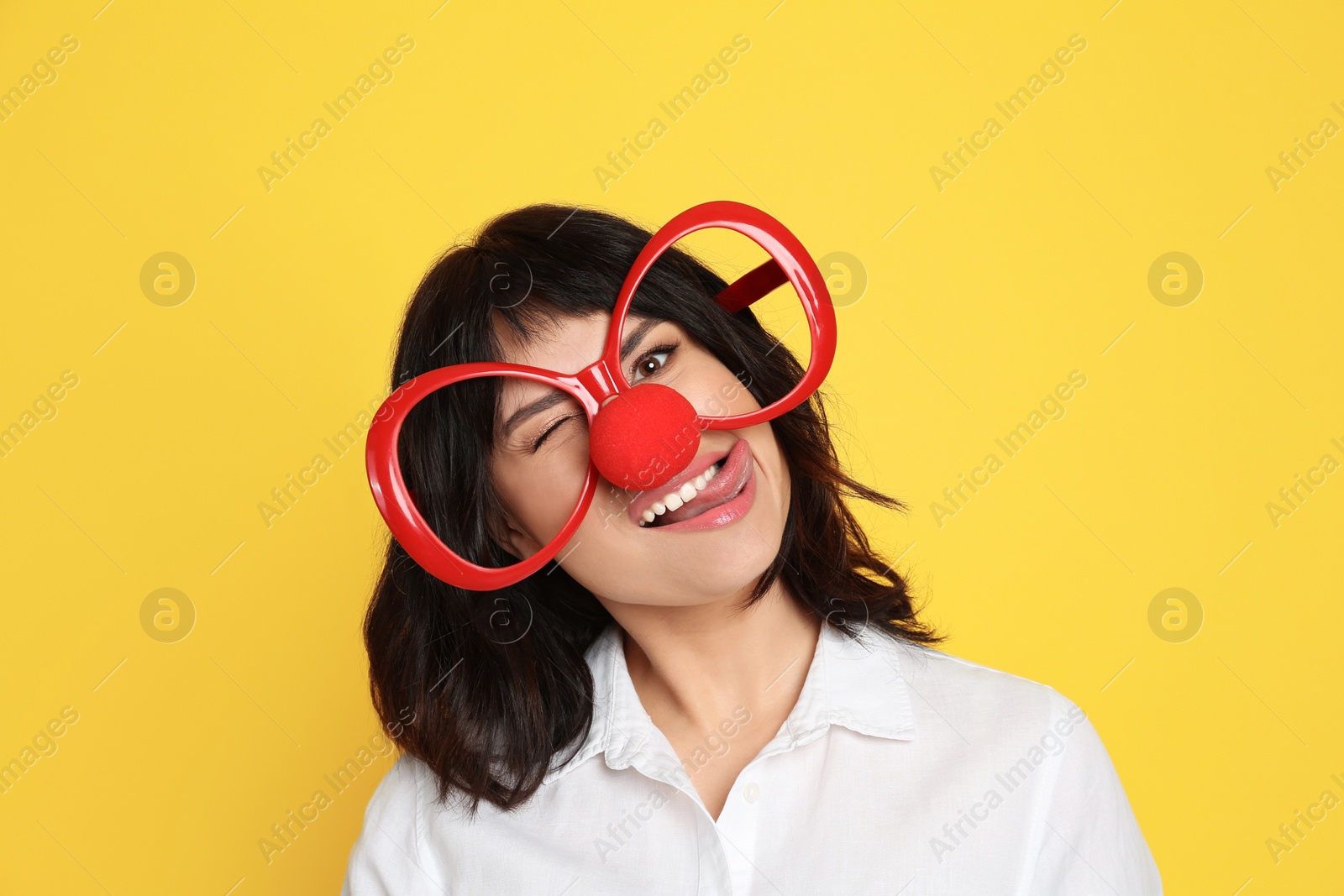 Photo of Funny woman with clown nose and large glasses on yellow background. April fool's day