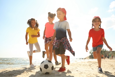 Cute children playing soccer at beach on sunny day. Summer camp