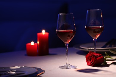 Photo of Beautiful table setting with glasses of wine, candles and rose in dark room. Romantic dinner for Valentine's day 