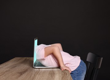 Internet addiction. Little girl getting into laptop against black background