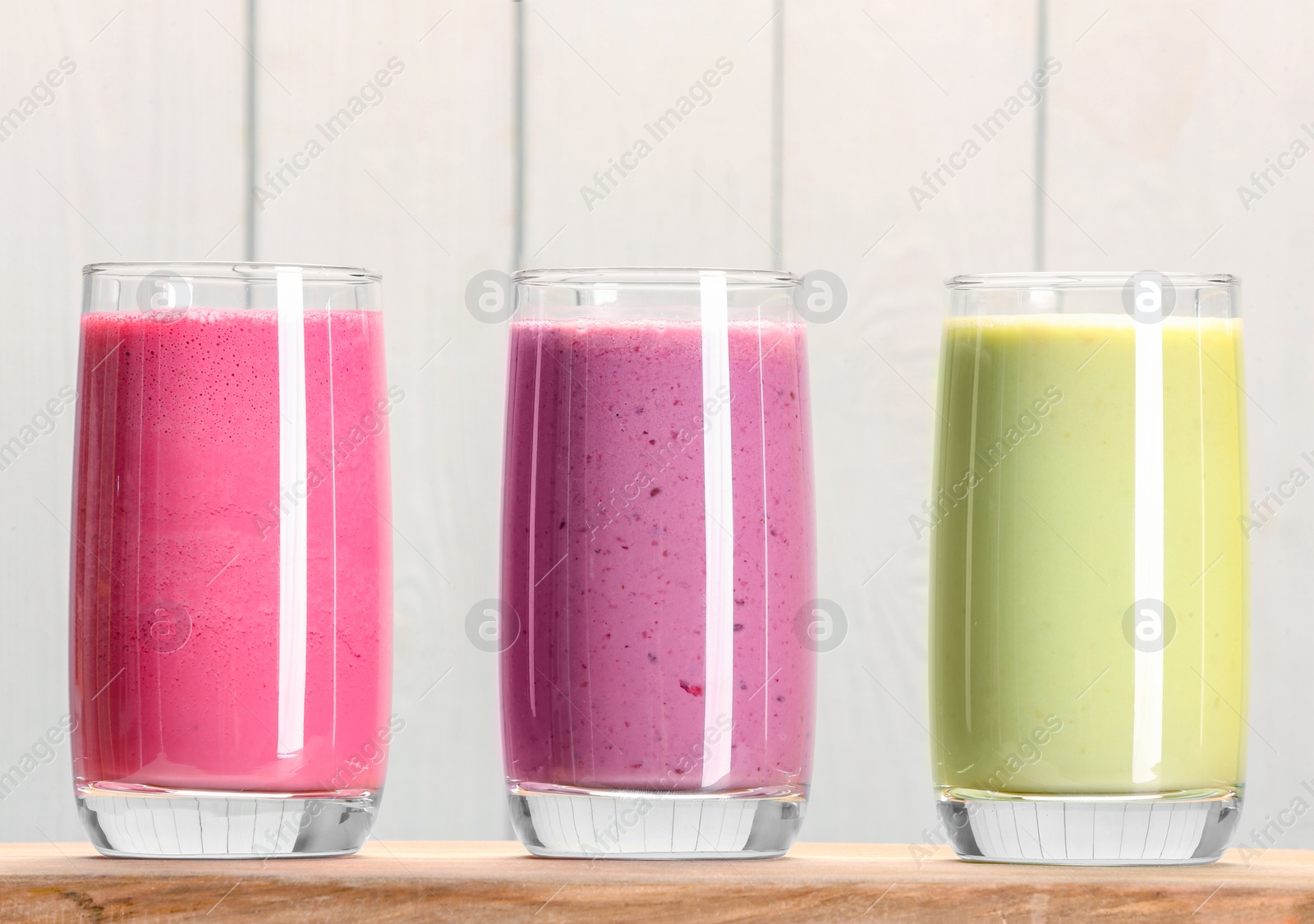 Photo of Board with many different tasty smoothies against white wooden background, closeup