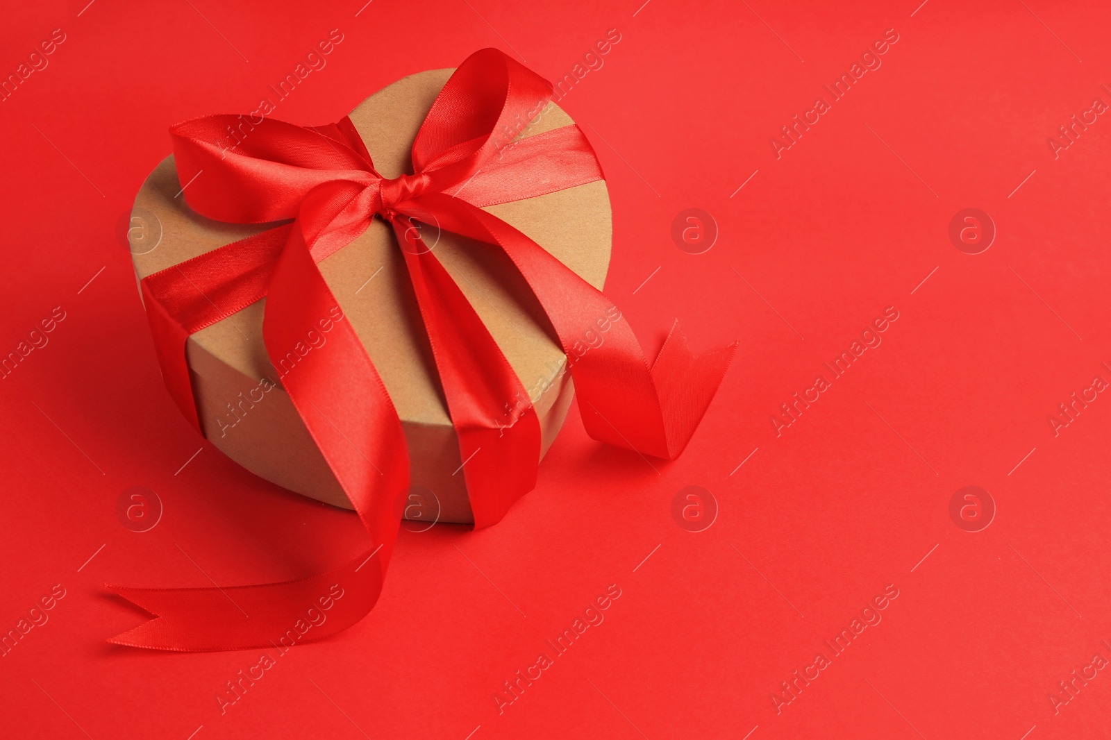 Photo of Beautiful heart shaped gift box with bow on red background, space for text
