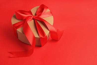 Beautiful heart shaped gift box with bow on red background, space for text