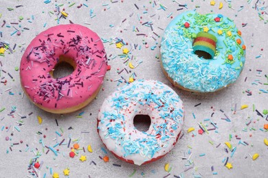 Photo of Sweet glazed donuts decorated with sprinkles on light grey table, flat lay. Tasty confectionery