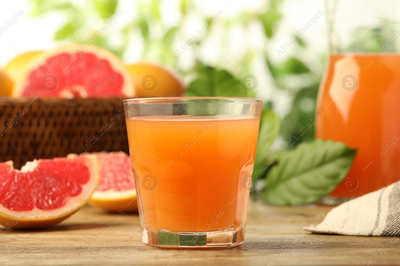 Photo of Glass of delicious grapefruit juice on wooden table against blurred background