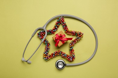 Photo of Greeting card for doctor with stethoscope, gift box and Christmas decor on green background, flat lay