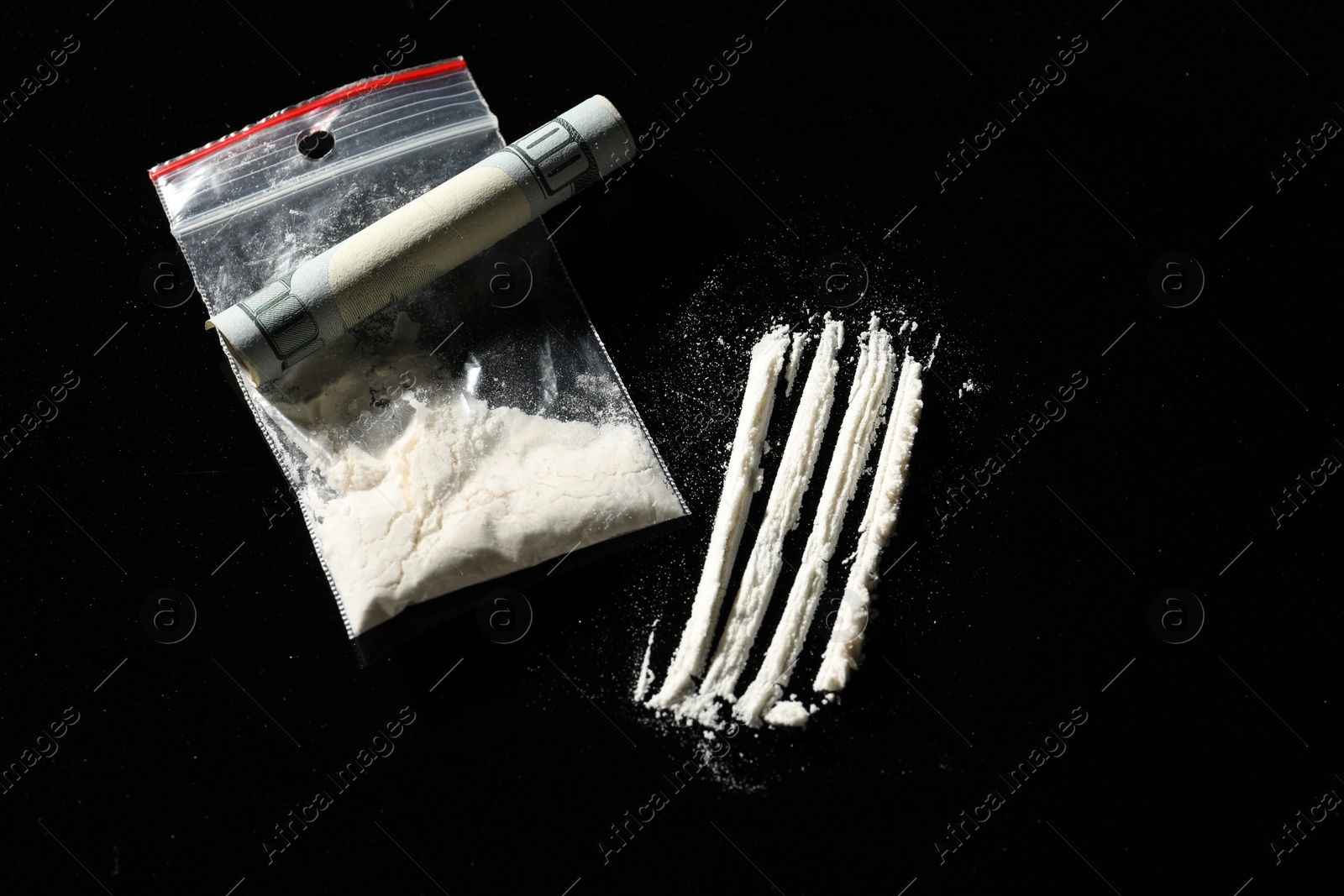 Photo of Drug addiction. Plastic bag with cocaine and rolled dollar banknote on black background, above view