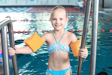 Photo of Little girl with swimming sleeves in indoor pool